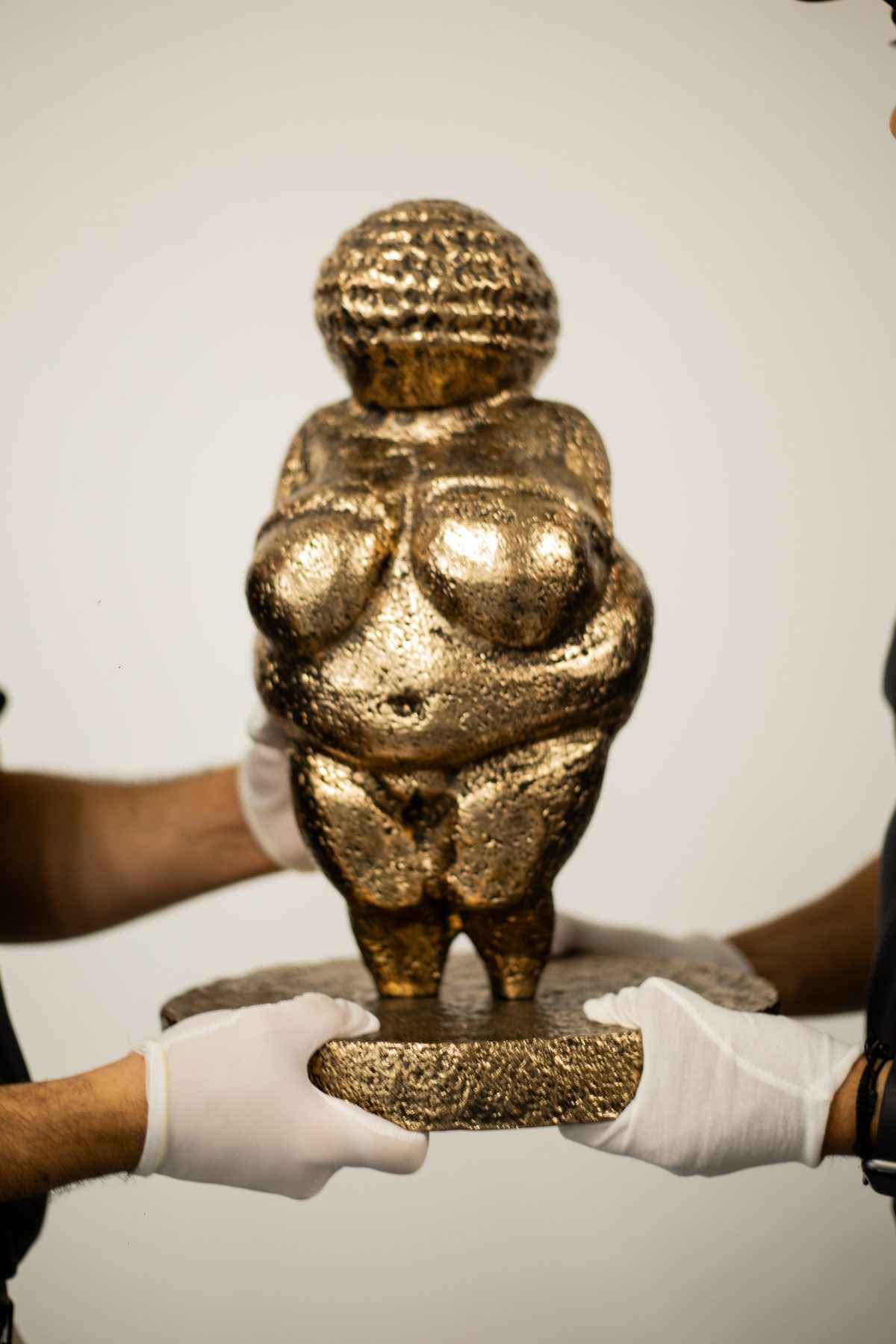 Gloved hands presenting a gilded sculpture